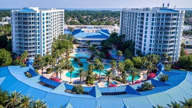A resort with multiple buildings, a central pool area, and surrounding palm trees.