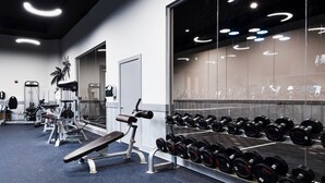 A gym with various exercise equipment, including dumbbells and benches, and a mirrored wall.
