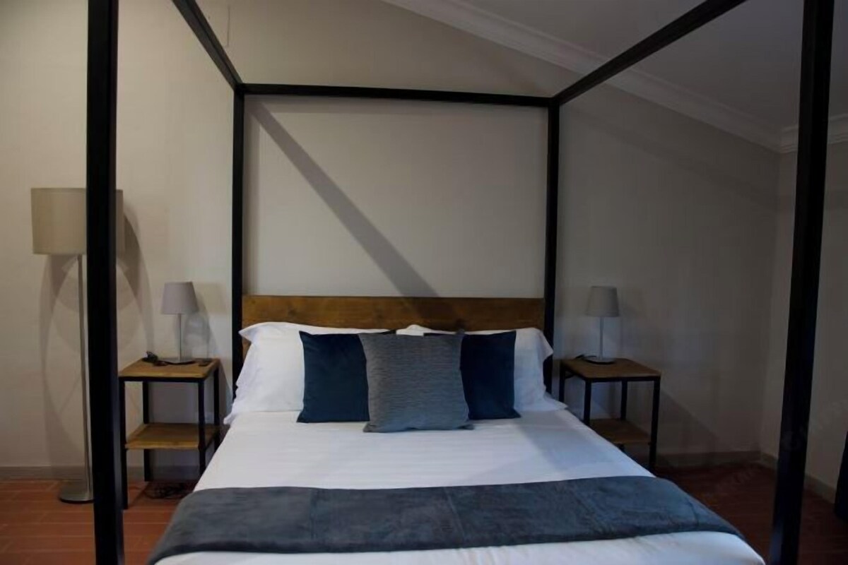 Una cama bien tendida con un cabecero de madera, dos mesitas de noche con lámparas y una lámpara de pie.