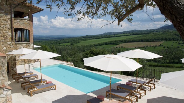 Zona junto a la piscina con sillones de descanso y sombrillas, con vistas a un paisaje verde.