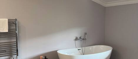 Un baño con una bañera independiente, un perchero y un pequeño armario de madera.