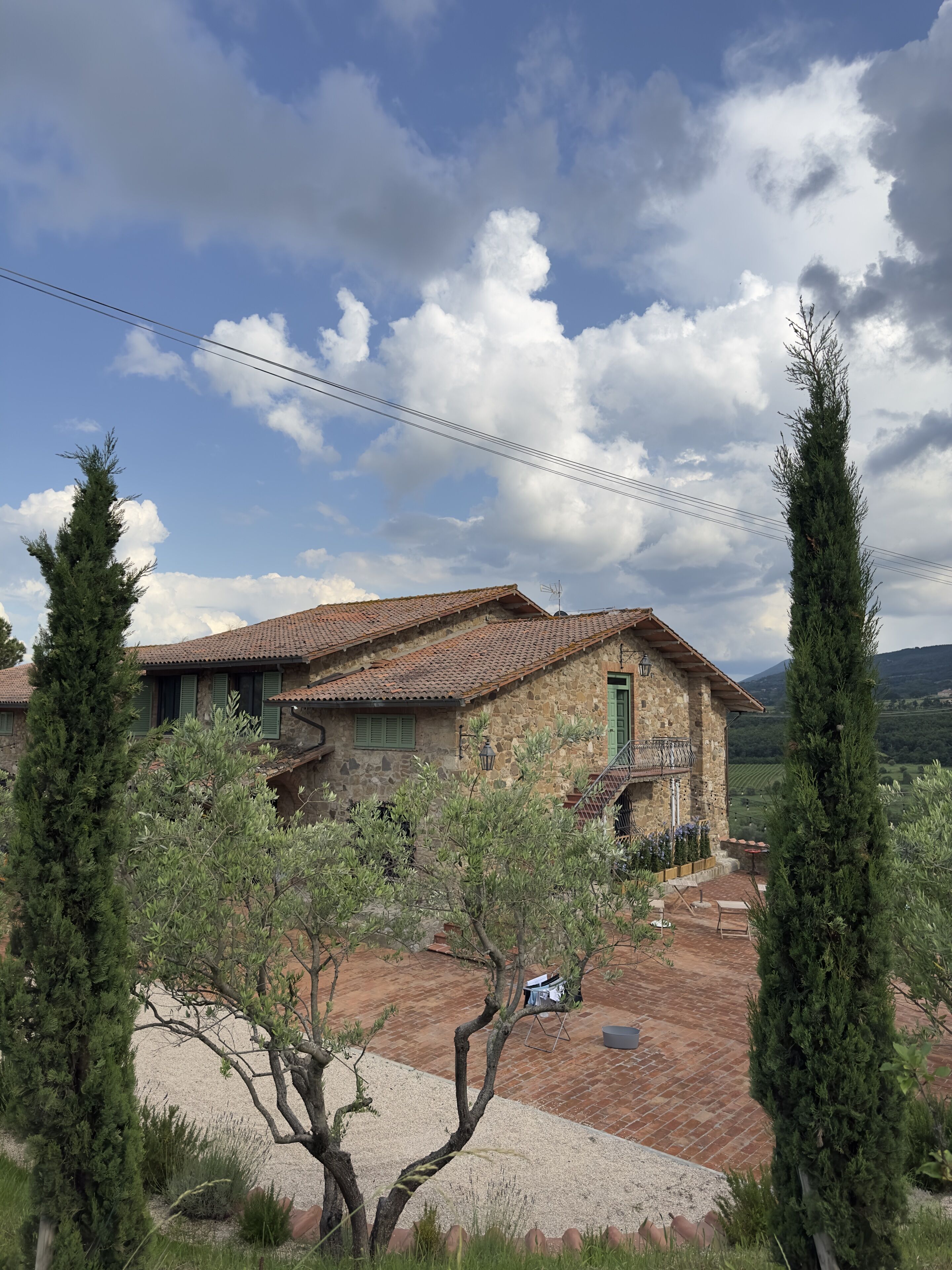 A stone house with a tiled roof, a gravel driveway, and a small garden with trees.
