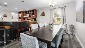A modern kitchen with a bar area, a dining table with chairs, and a chandelier.