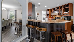 A modern kitchen with a central island, bar stools, wooden cabinets, and a dining area with a table and chairs.