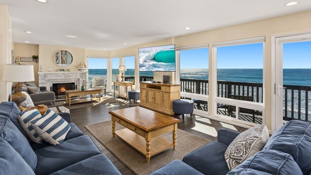 A spacious living room with a large window overlooking the ocean, a fireplace, and a comfortable seating area. - Oceanfront Family Getaway | BBQ | Outdoor Seating (Oceanside)