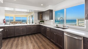 A modern kitchen with dark wood cabinets, stainless steel appliances, and large windows offering ocean views. - Oceanfront Family Getaway | BBQ | Outdoor Seating (Oceanside)