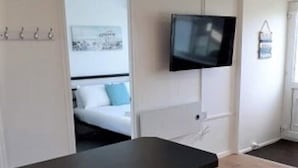 A modern room with a long table, two bar stools, a flat-screen TV mounted on the wall, and a bed with a blue pillow. - Exceptional Chalet 5 min walk to beach, short drive to the Broads & Gt Yarmouth (Yarmouth)