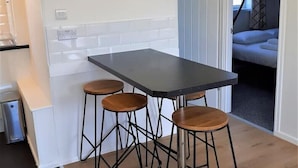 A compact kitchen with a dark countertop, three wooden stools, and a white tiled backsplash. - Exceptional Chalet 5 min walk to beach, short drive to the Broads & Gt Yarmouth (Yarmouth)