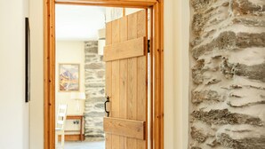 A wooden door with a handle, leading to a room with a stone wall and a painting on the wall.