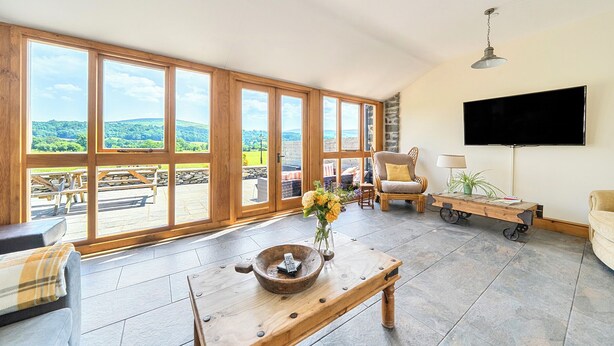 A spacious living room with large windows, a flat-screen TV, and a wooden coffee table.