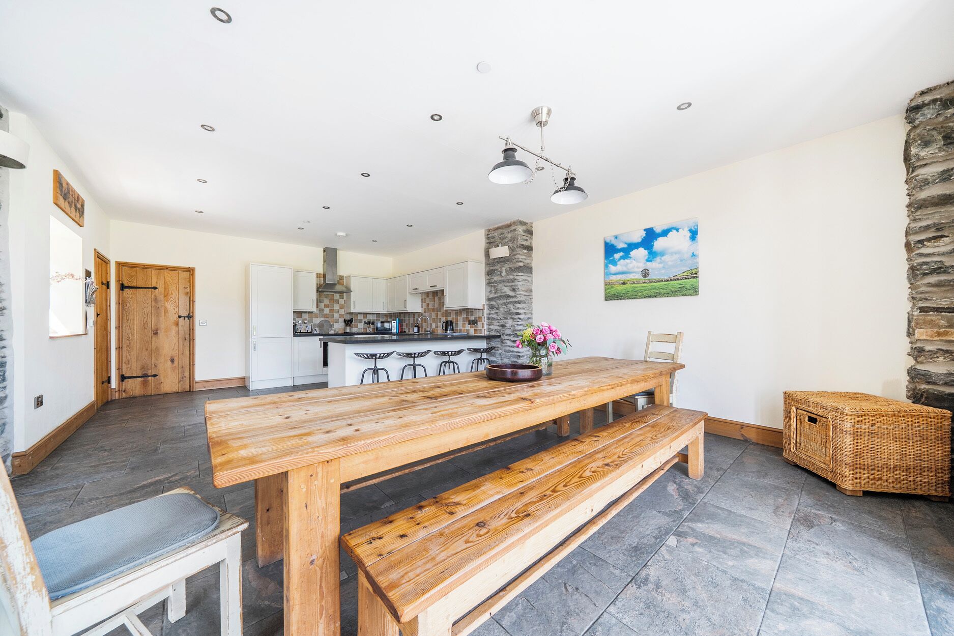 A spacious kitchen with white cabinets, a central island with bar stools, a stone accent wall, and a dining area with a wooden table and bench.