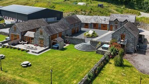 A stone building with a circular driveway, a large barn, and a grassy area with picnic tables.