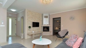 A modern living room with a fireplace, a round coffee table, and a grey sofa. - Villa mit Pool und Klimaanlage (Kosinožići)
