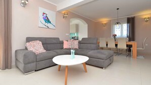 A modern living room with a grey sofa, a white coffee table, and a dining area with a wooden table and chairs. - Villa mit Pool und Klimaanlage (Kosinožići)