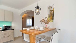 A modern kitchen with a wooden table, white chairs, and a hanging light fixture. - Villa mit Pool und Klimaanlage (Kosinožići)