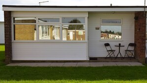 A small building with a garage door, two windows, and a small patio area with two chairs and a table.