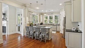 A modern kitchen with a central island, bar stools, pendant lighting, and a view of the outdoors. - 5 BR Seabrook Oasis on Ocean Winds Course- Private Pool, Club Access! (Seabrook Island)