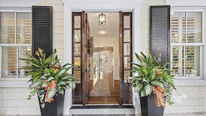 A front entrance with a wooden door, a black planter with plants, and a doormat. - 5 BR Seabrook Oasis on Ocean Winds Course- Private Pool, Club Access! (Seabrook Island)