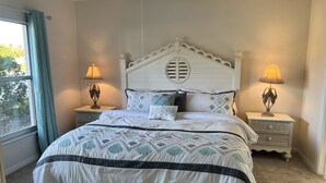 Un dormitorio con una cama, dos mesitas de noche, una ventana con cortinas y vistas a zonas verdes.