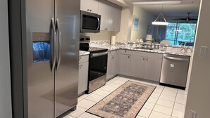 Una cocina moderna con electrodomésticos de acero inoxidable, microondas, horno y lavavajillas, y vistas al exterior.
