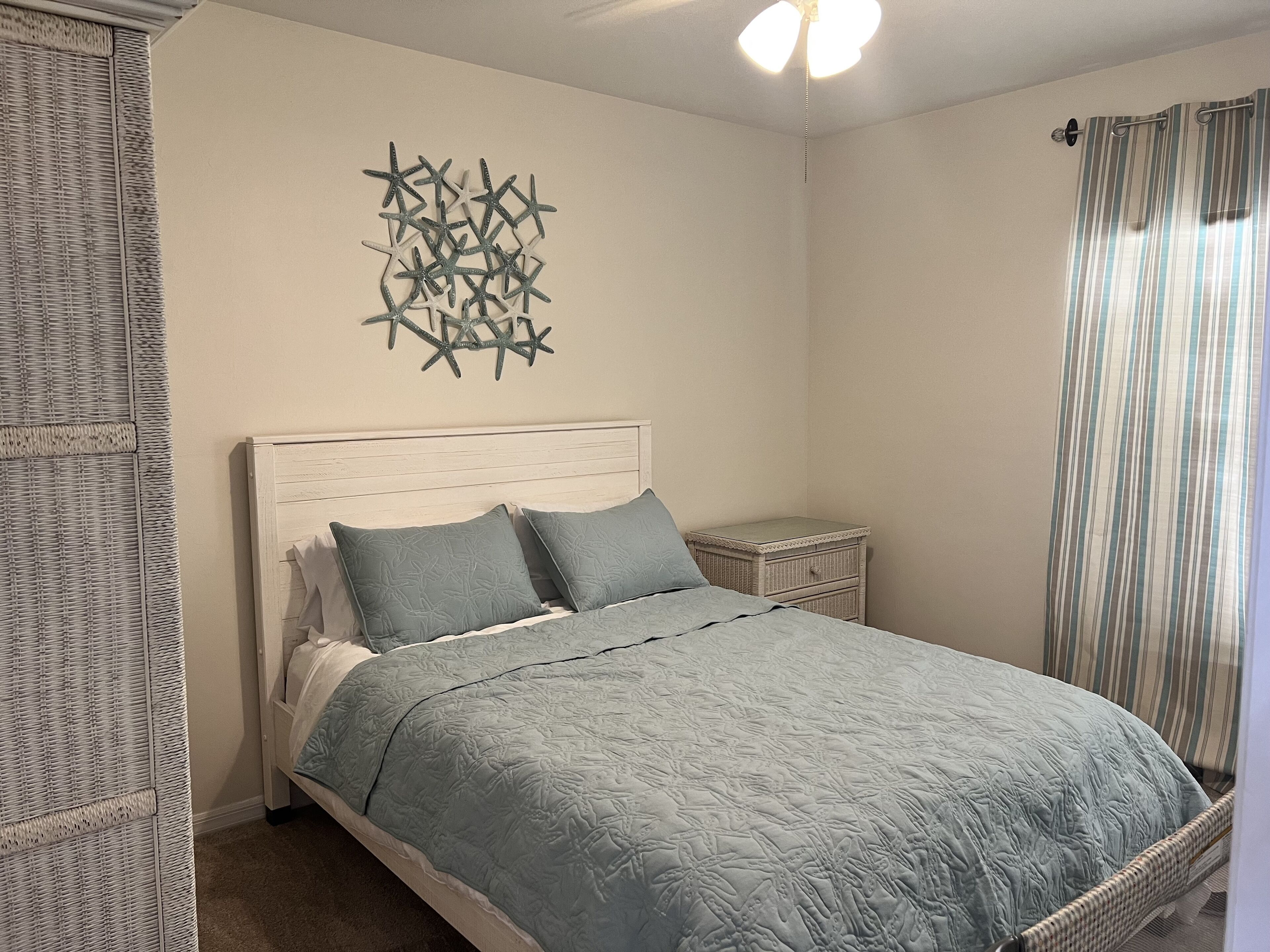 A bedroom with a bed, a nightstand, a wall art piece, and a window with curtains.