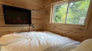 Une chambre dans un chalet en bois, avec un lit, un téléviseur fixé au mur et une fenêtre donnant sur un paysage verdoyant.