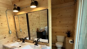 Une salle de bain rustique, avec des murs en bois, comprenant deux lavabos, un miroir, des toilettes et un espace douche.
