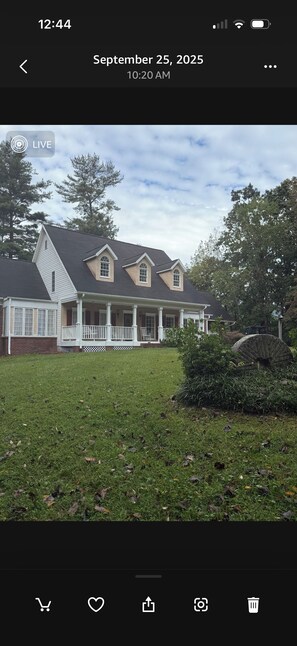 A two-story house with a front porch, a lawn, and a stone structure in the yard.