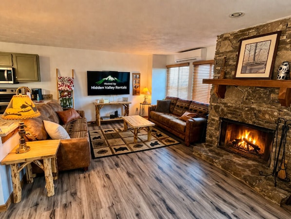 A cozy living room with a stone fireplace, a television, and a wooden coffee table.