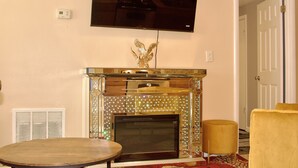 Una sala de estar con chimenea, un televisor de pantalla plana sobre ella y una puerta que da a otra habitación.