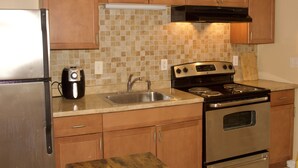 Una cocina con armarios de madera, un refrigerador de acero inoxidable, una cafetera, un fregadero y una estufa.