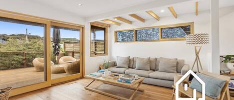 Amplia sala de estar con un gran ventanal corredero que da a una terraza exterior, un conjunto de sofás, una mesa de centro y una lámpara de pie.