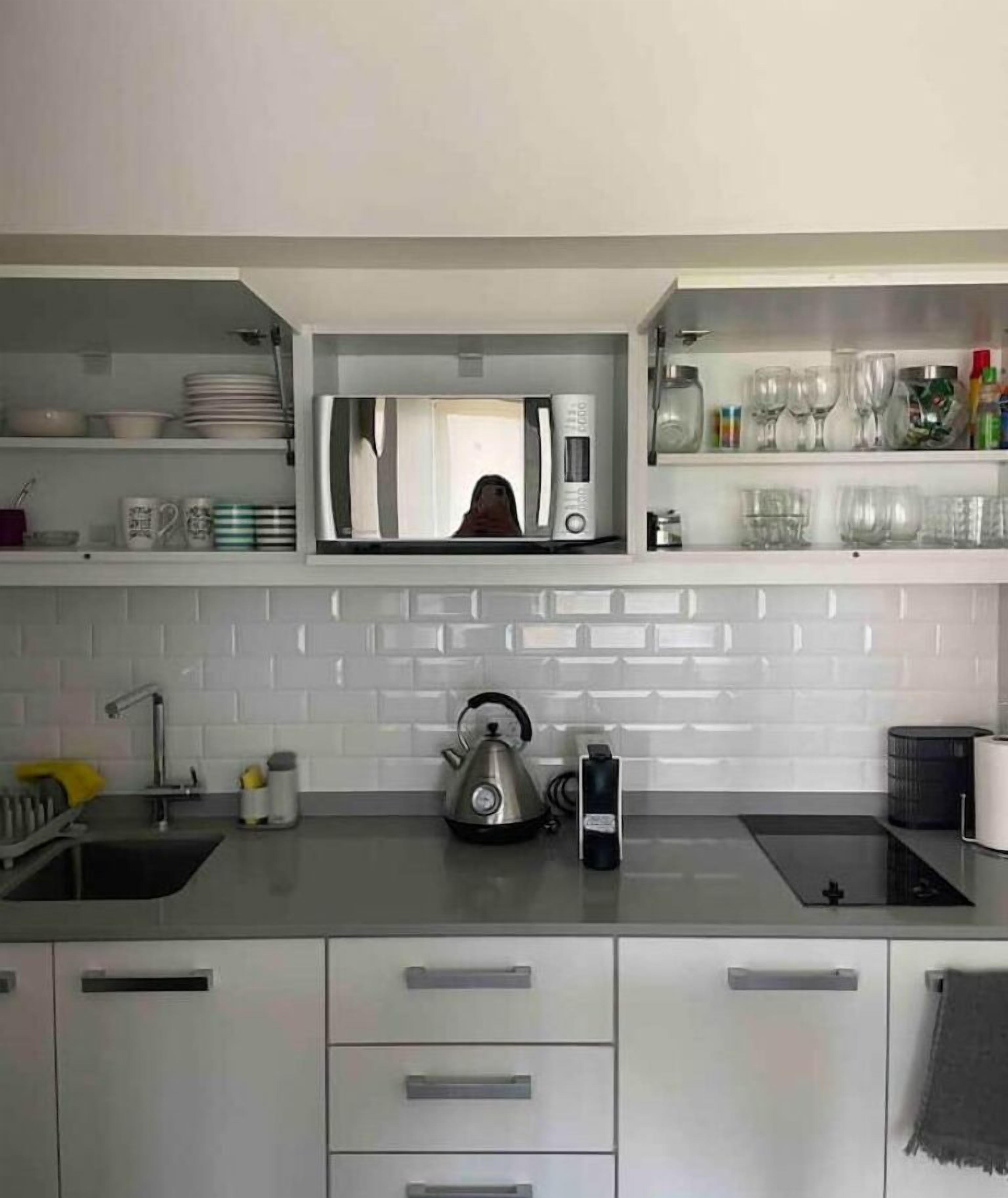 Una cocina moderna con armarios blancos, hervidor, cafetera y microondas.
