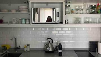 Una cocina moderna con armarios blancos, hervidor, cafetera y microondas.