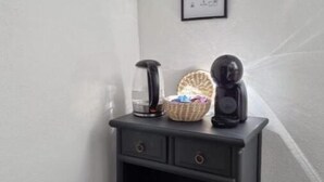 A small black nightstand with a coffee maker, a glass of water, and a basket. - Dream Day Cottages #5
 (Tutu)