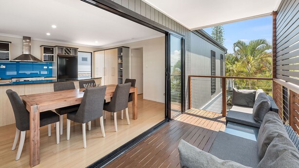 A modern kitchen with a dining area, a balcony with a sofa, and a view of the outdoors. - 22 Seaview Terrace Moffat Beach (Moffat Beach)