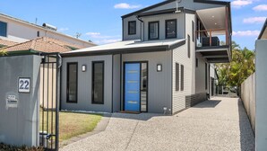 A modern two-story house with a blue door, a small front yard, and a gravel driveway. - 22 Seaview Terrace Moffat Beach (Moffat Beach)