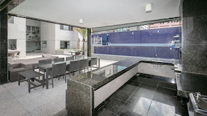 A modern kitchen with a large island, a dining area with outdoor seating, and a view of a blue-tiled pool.