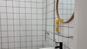 A bathroom with white tiled walls, a white sink, a mirror, and a shower. - Dream Day Cottages #7
 (Tutu)