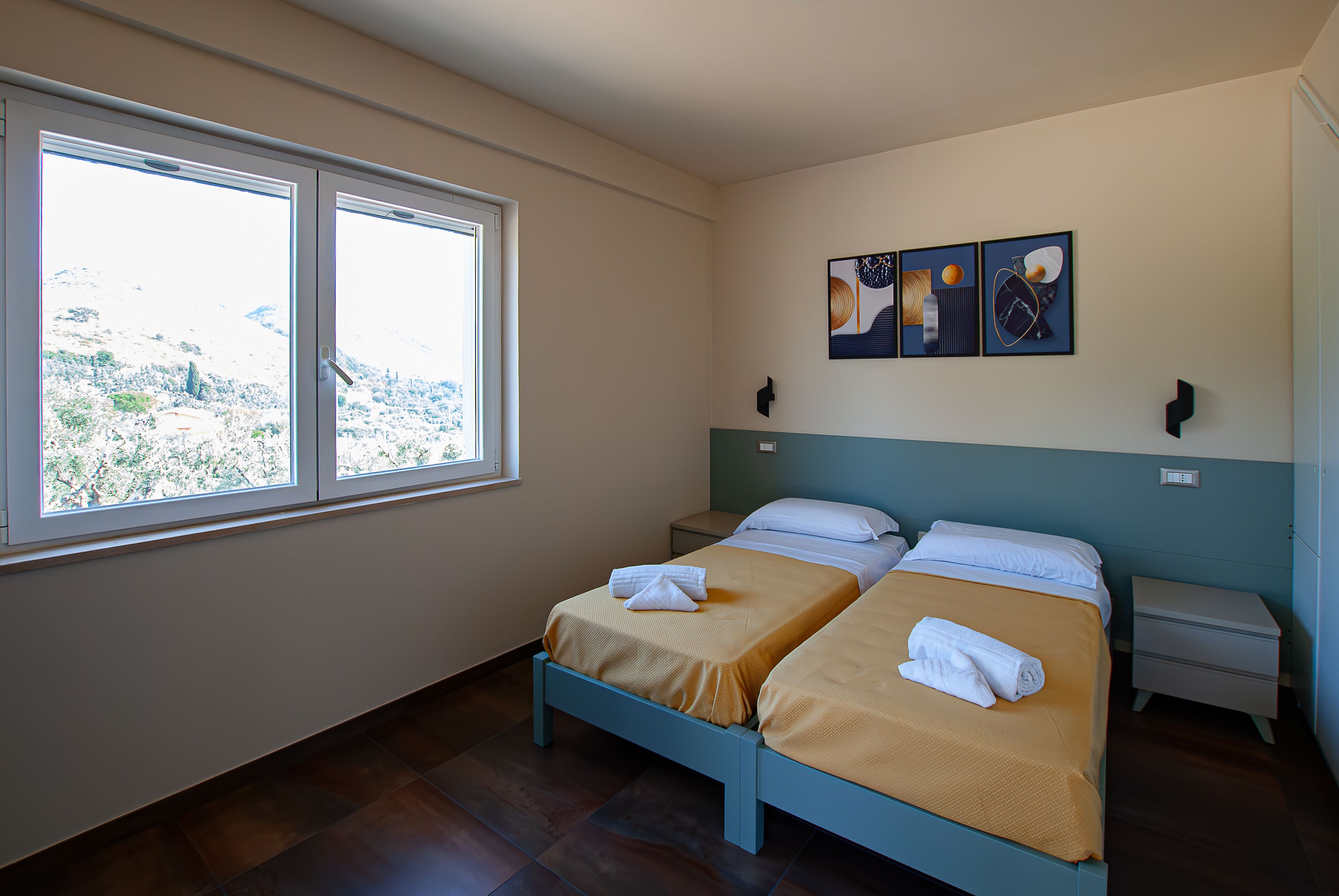 Une chambre avec deux lits, une fenêtre donnant sur la ville et des œuvres d’art accrochées au mur.