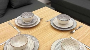Une table à manger dressée avec quatre assiettes, chacune ornée d’un motif décoratif, et des couverts assortis.
