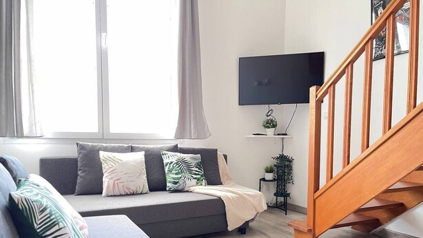 Un salon moderne avec un canapé gris, un escalier en bois et un téléviseur à écran plat fixé au mur.
