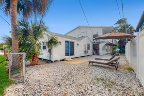 A single-story house with a covered patio area, a gravel driveway, and a chain-link fence.
