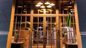 Das Außengebäude von La Galerie mit einer auffälligen beleuchteten Signatur, großen Fenstern und Pflanzgefäßen am Eingang.