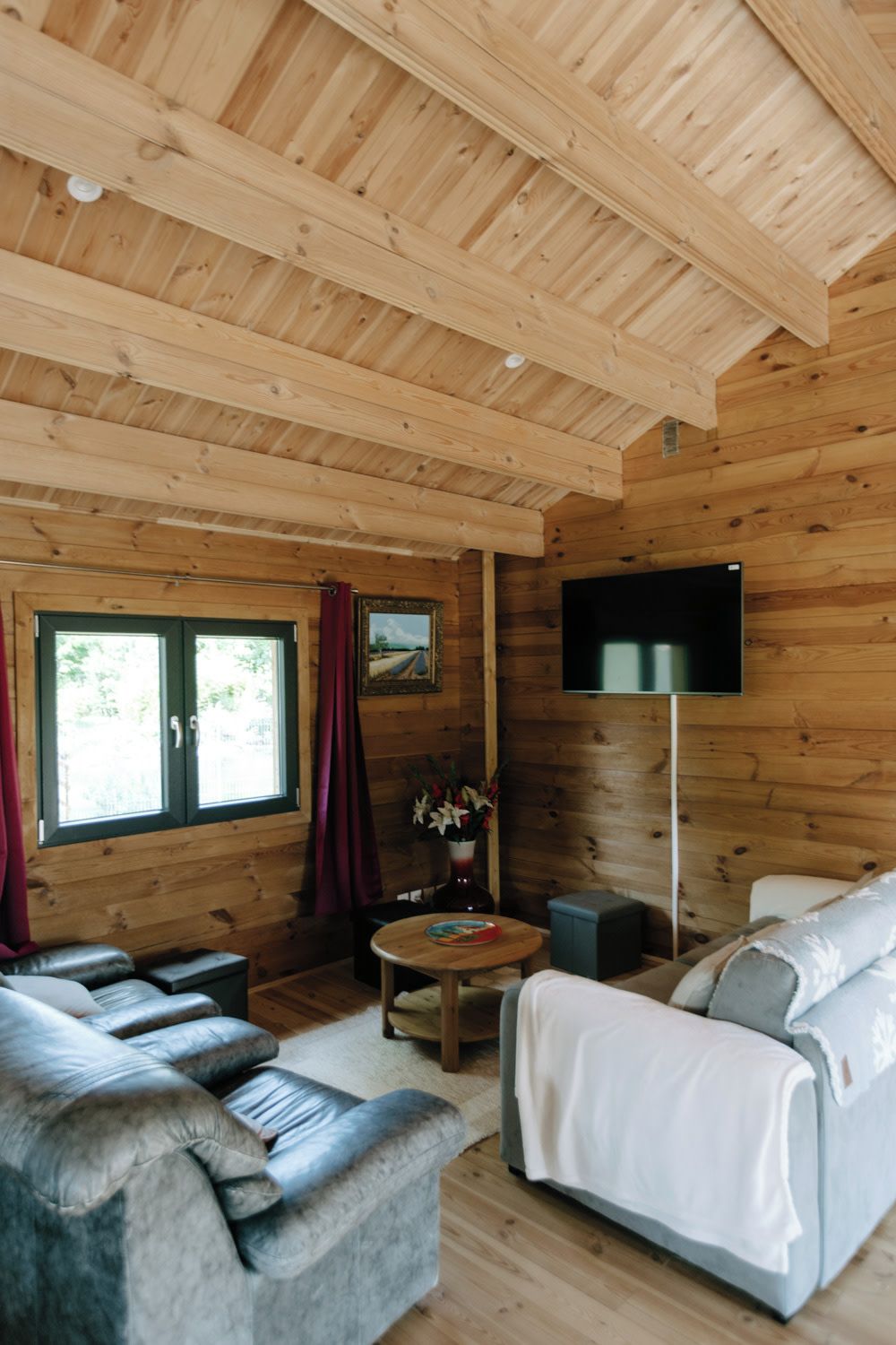 A wooden cabin interior with a sofa, a television, and a window with curtains.