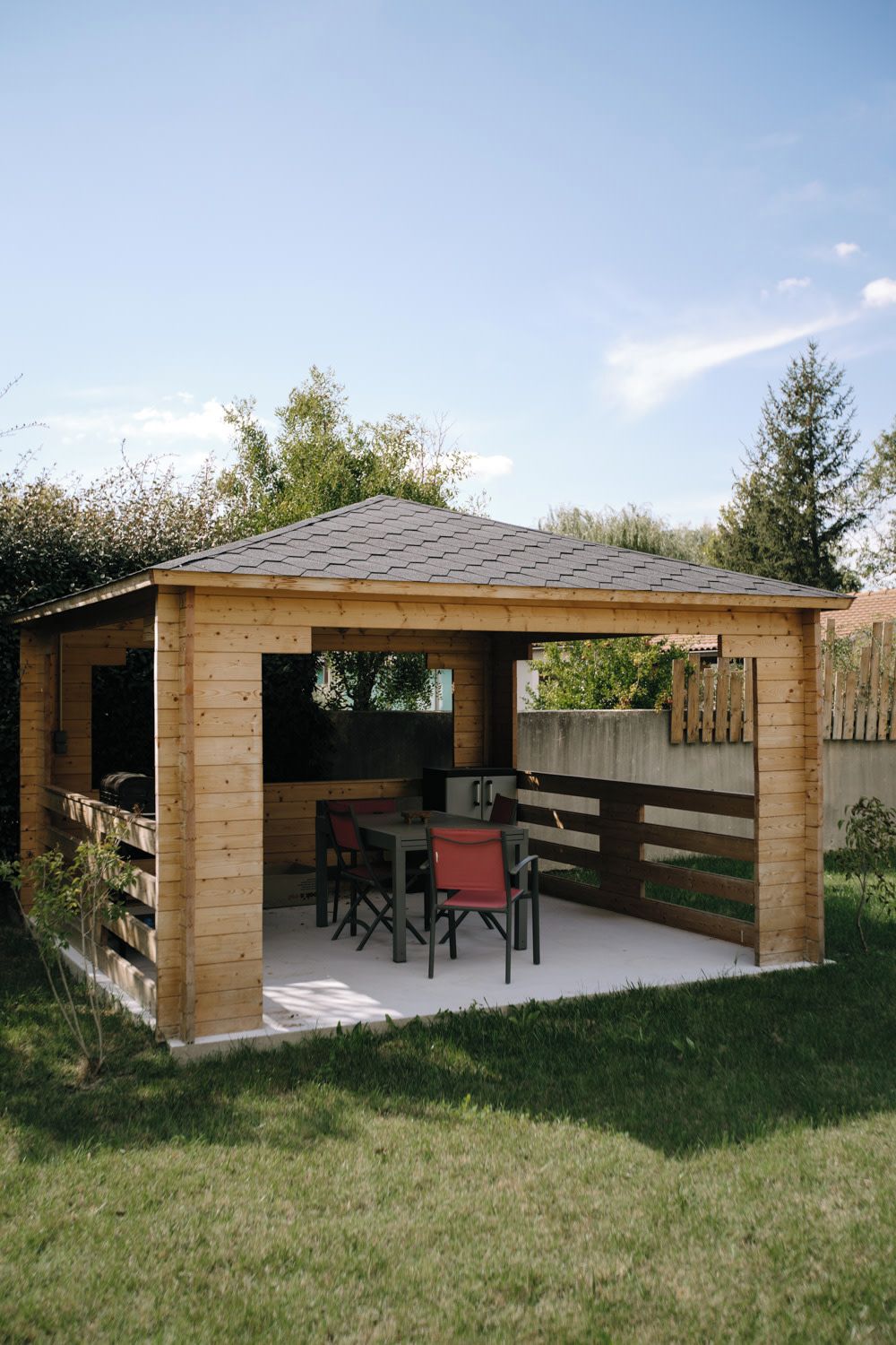 A wooden gazebo with a tiled roof, a table, and chairs.