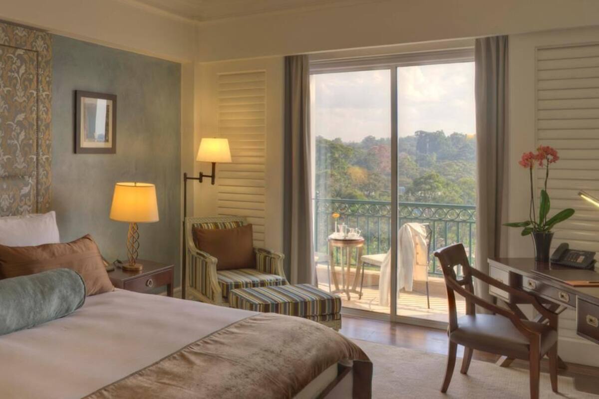 A hotel room with a large bed, a desk, a chair, a small table, and a balcony with a view.