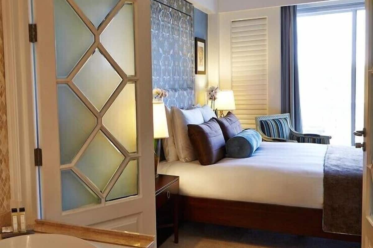 A hotel room with a large bed, a nightstand, a lamp, and a window with blinds.