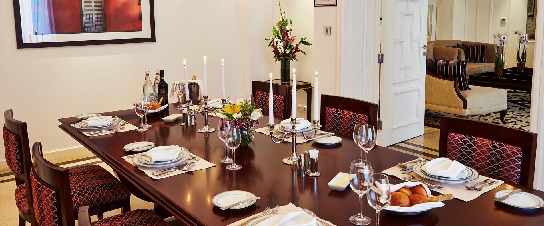 A formal dining room with a long table set for a meal, featuring white plates, silverware, and candles.