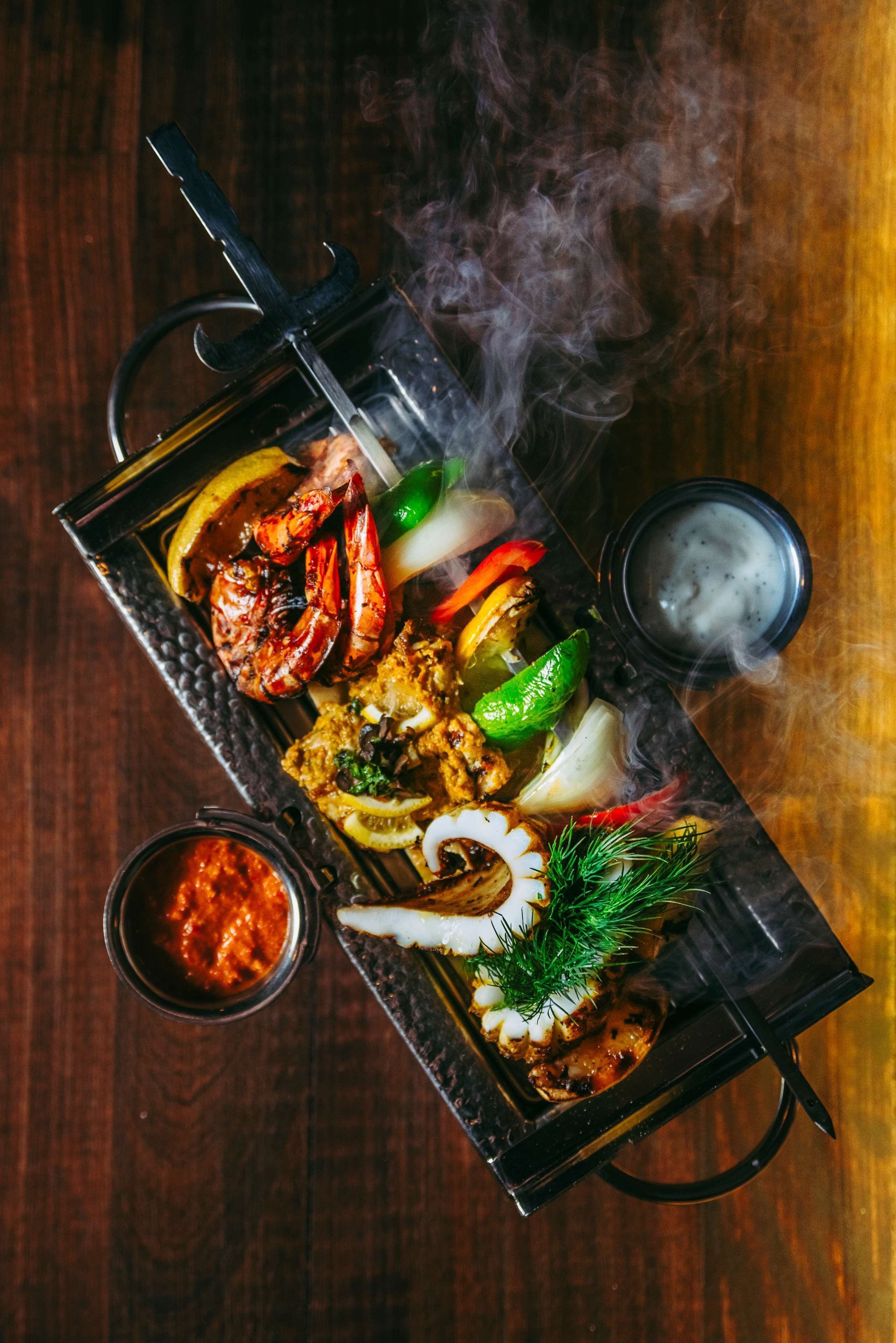 A tray of grilled seafood and vegetables on a wooden table.